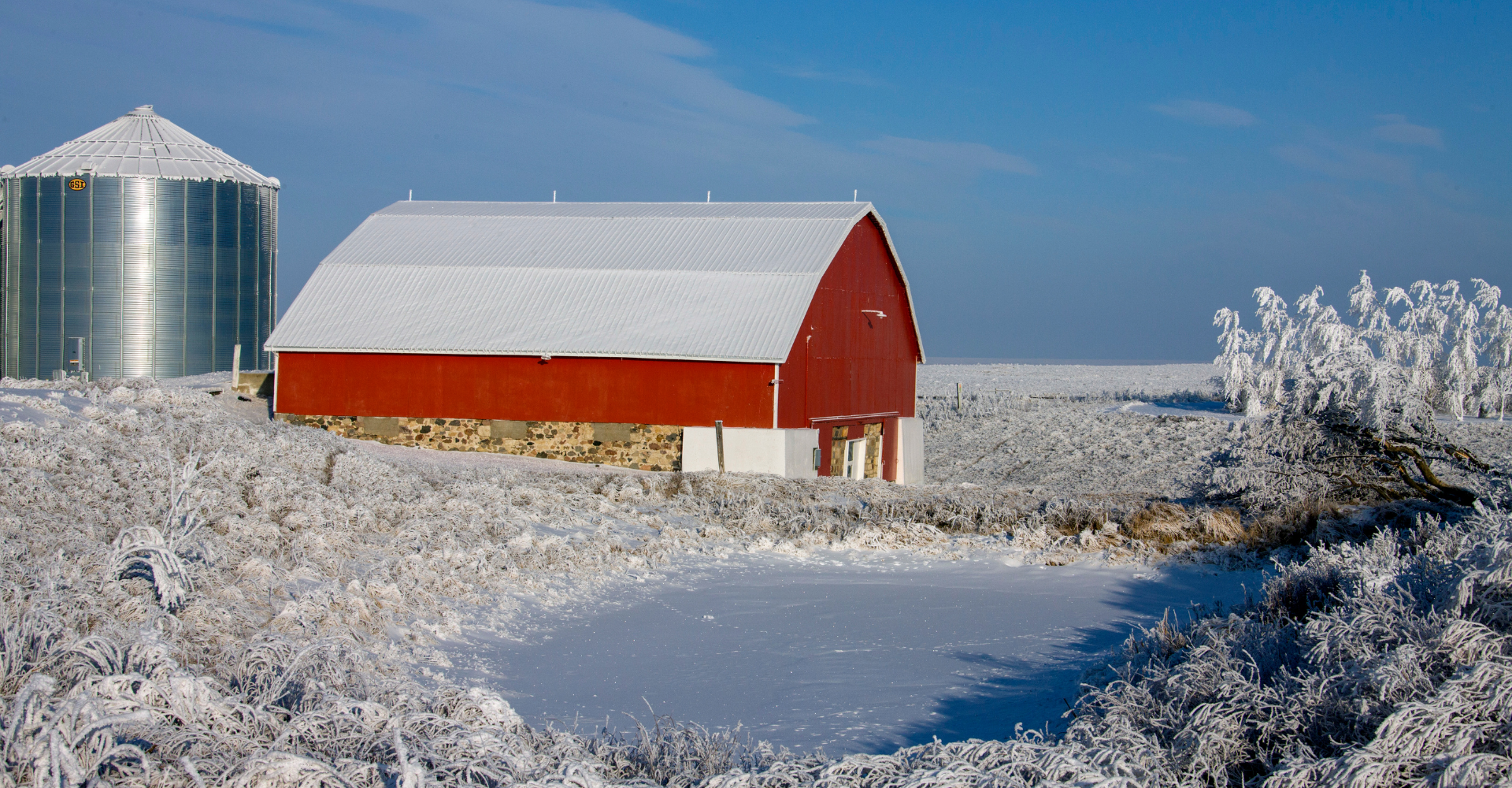A reb barn covered in snow in the middle of a snowy farm. Highlights the best time to sell Saskatchewan Farmland is in the winter!